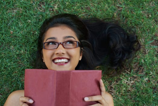 Woman, happy and reading book on grass, literature and smiling for fiction or fantasy story. Female person, nature and relaxing on lawn for knowledge, textbook and student studying in garden outdoors