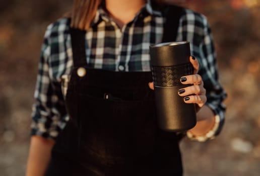 Hipster woman enjoys aroma and taste of fresh coffee. Drinking thermos in forest