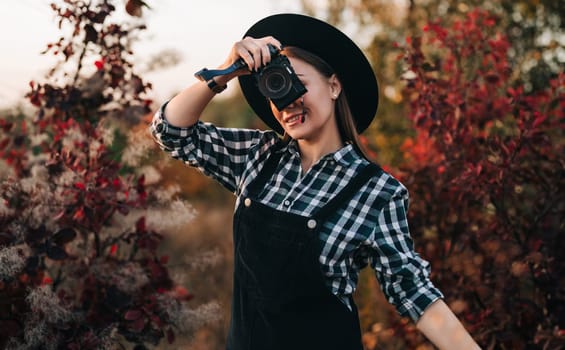 Young pretty woman takes pictures with DSLR camera outdoors on autumn background