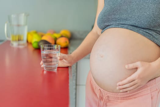 Embracing the vital benefits of water during pregnancy, a pregnant woman stands in the kitchen with a glass, highlighting hydration's crucial role in maternal well-being