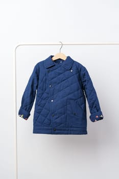 Blue quilted kids coat on hanger against white wall