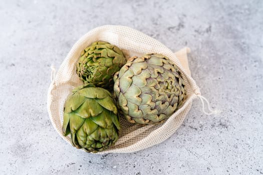 Top view of artichoke in linen eco bag on table. Flat lay of Healthy food vegetables.