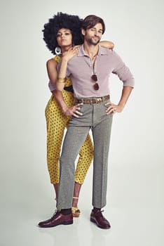 Couple, portrait and fashion in confidence for style, outfit or clothing on a gray studio background. Young interracial man and woman in stylish retro or vintage pants, shirt or jumpsuit with jewelry.