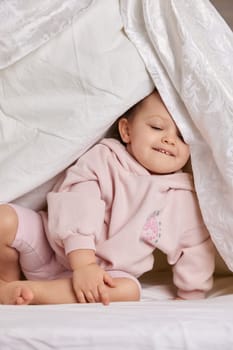 cute baby looks out from under the blanket