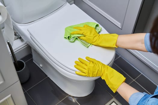Close-up hands in protective gloves cleaning toilet in bathroom