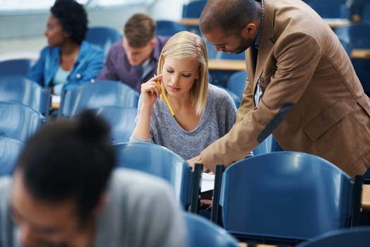 University, helping and professor with student in classroom studying for test, exam or assignment. Education, learning and teacher talking and explaining college information to woman in lecture hall.