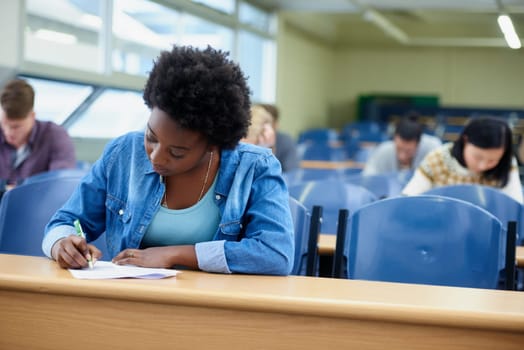 Writing, college and black woman student in classroom studying for test, exam or assignment. Education, university and African female person working on project with knowledge in lecture hall.