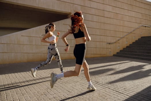 Side view of women athlete running side by side along an outdoor track on buildings background