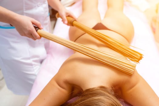 Woman masseuse doing double samurai massage with bamboo brooms in spa. Relaxing massage concept