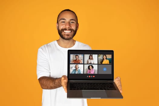 A beaming man with a beard confidently holds out a laptop showing a screen