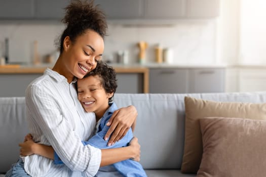 Joyous black preteen boy in warm embrace with his loving mother, radiating happiness and familial love in cozy home environment, sitting together on sofa