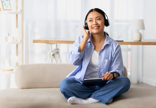 Happy young korean woman using wireless headphones and tablet