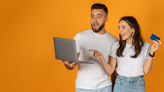 A man and a woman holding a laptop and a credit card look amazed