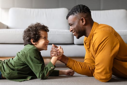Black father and son engaging in friendly arm wrestling match at home