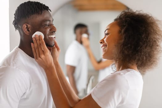 Black woman applying aftershave lotion to husband's face in bathroom