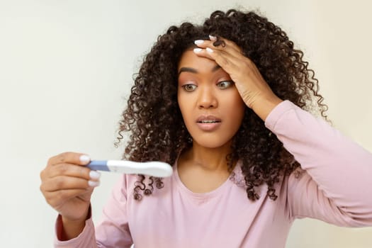 Surprised young black woman holding pregnancy test and looking with disbelief