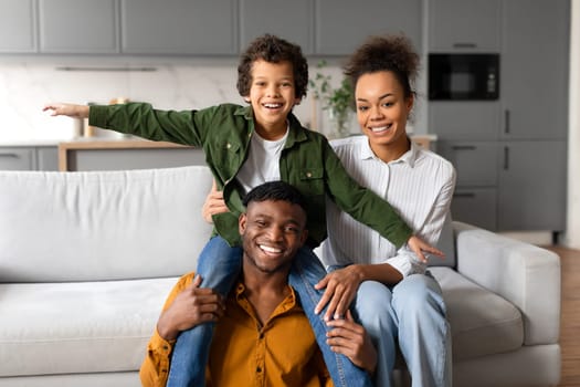 Happy black family moment with son riding on father's shoulders, mother supporting