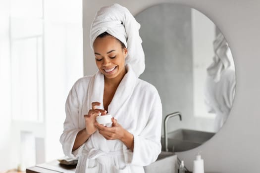 black young lady opens jar of cream moisturizer in bathroom