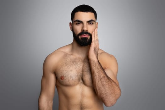 Attractive millennial topless arab guy touching his beard