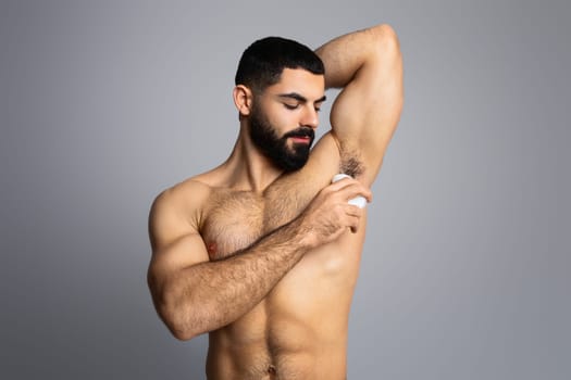 Muscular handsome middle eastern shirtless man using antiperspirant