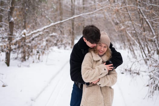 A young couple walks in the park in winter. Guy and girl hugging outdoors.