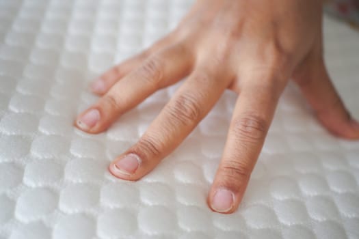 Hand touching and pressing orthopedic mattress on bed.