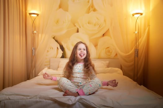 Happy small young child girl doing yoga in bed room or in hotel