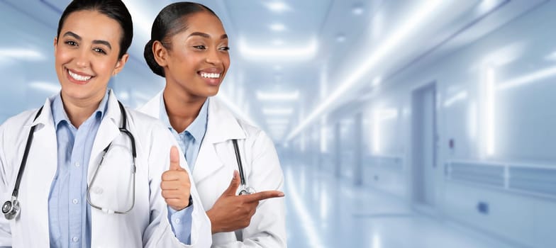 Two happy healthcare workers in white lab coats give a thumbs up in a hospital corridor