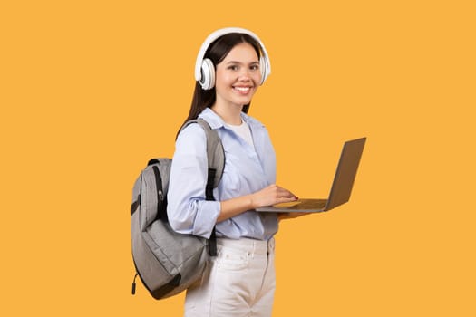 Smiling female student with laptop and headphones looking at camera