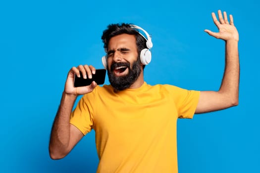 Joyful indian man singing with phone and headphones