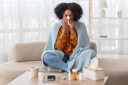 Woman feeling sick, sneezing into a tissue, sitting cross-legged on a sofa