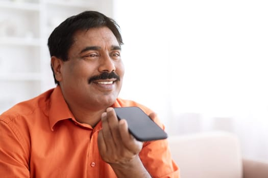 Mature indian man recording voice message, using smartphone