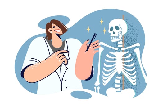 Woman doctor is teaching anatomy lesson for students of medical college, standing near skeleton