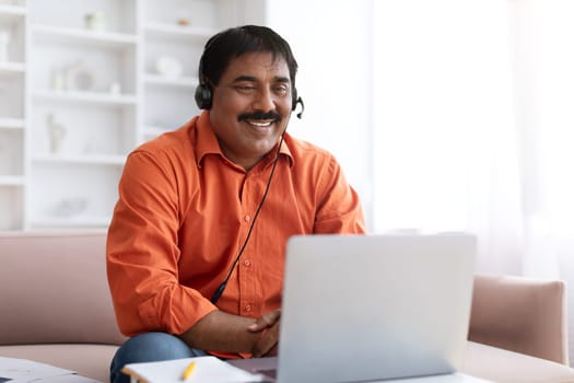 Excited mature indian man with headset using laptop at home
