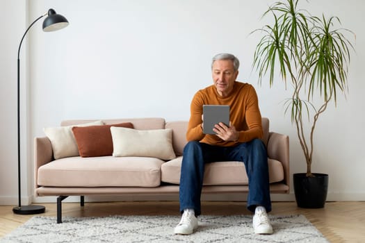 Relaxed mature man chilling at home, using tablet