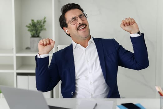 Ecstatic businessman in blue suit with eyes closed and fists pumped celebrates a victory