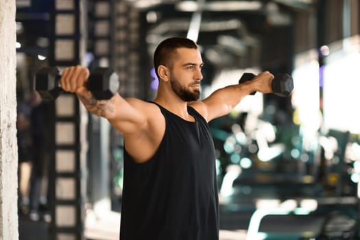 Portrait Of Motivated Young Man Training With Dumbbells At Gym