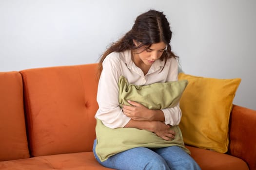 Young woman gripping pillow tightly to her stomach, feeling stressed