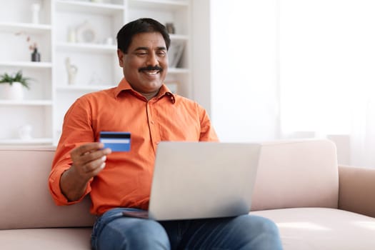 Mature indian man using laptop and credit card at home