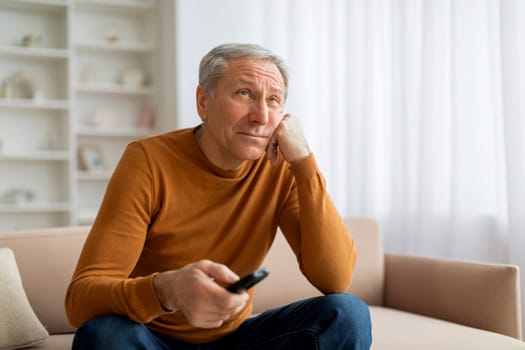 Unhappy senior man with remote control sitting on couch