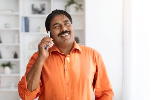 Cheerful mature indian man have phone conversation at home office