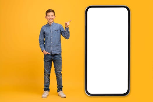 Check This. Happy teen boy pointing at big smartphone with blank screen