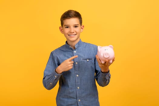 Happy excited teen boy pointing at piggy bank and looking at camera