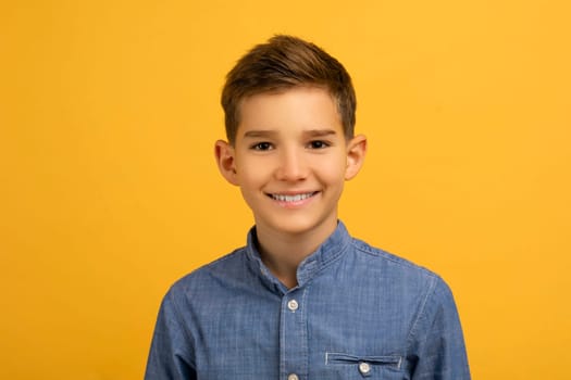 Happy teen boy with charming smile posing against vibrant yellow studio background