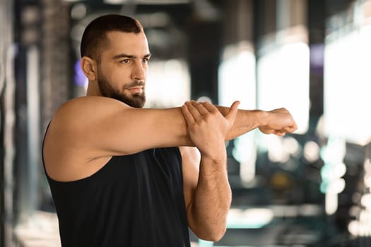 Portrait Of Athletic Young Man Stretching Arm Muscles At Gym