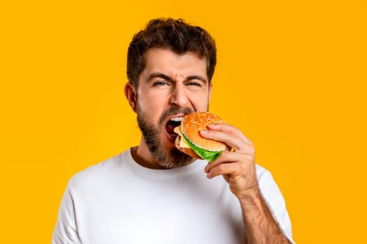 Hungry Guy Taking Bite Of Burger On Yellow Backdrop, Closeup