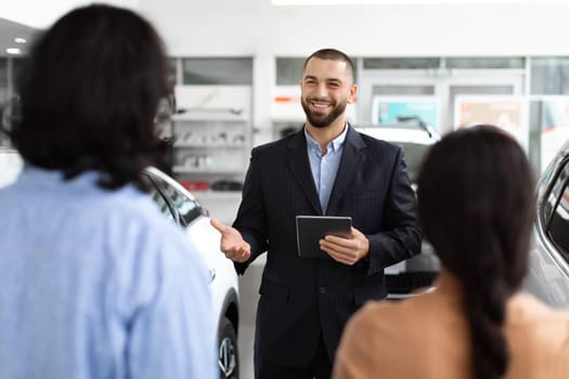 Professional car salesman consulting young couple at dealership salon