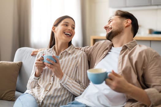 Happy european couple sharing joke over coffee on the couch