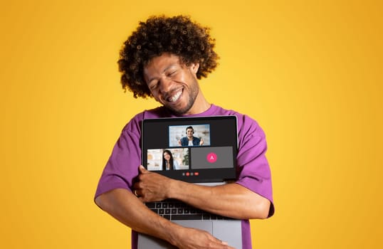 A man with curly hair joyfully hugs his laptop displaying a video conference
