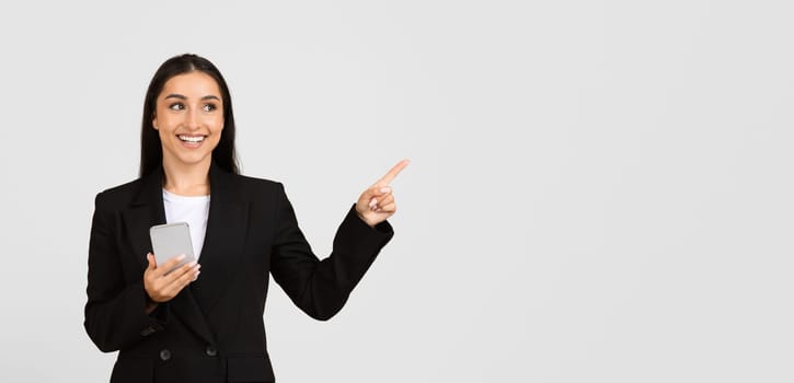 Smiling european businesswoman with phone pointing away at free space